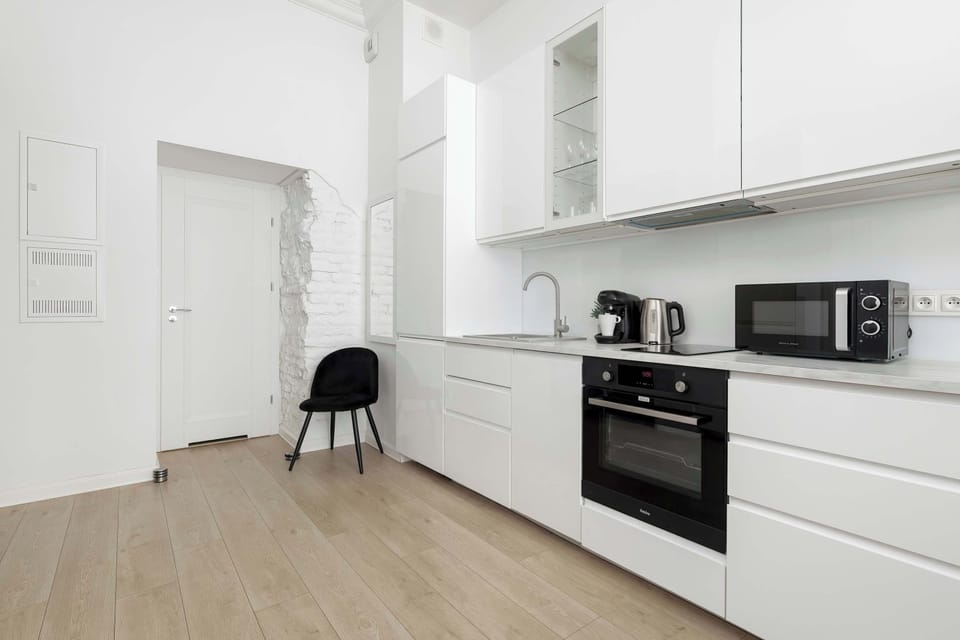 The entrance hallway features white walls and light-colored flooring, leading directly into the open kitchen area. A black chair placed against the wall serves as a functional accent in the minimalist corridor.