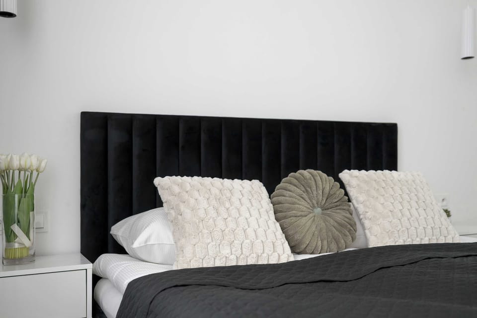 A close-up of the bed reveals textured grey and white pillows resting against a luxurious, vertical-tufted black headboard. The soft lighting emphasizes the calm and restful atmosphere of the sleeping space.