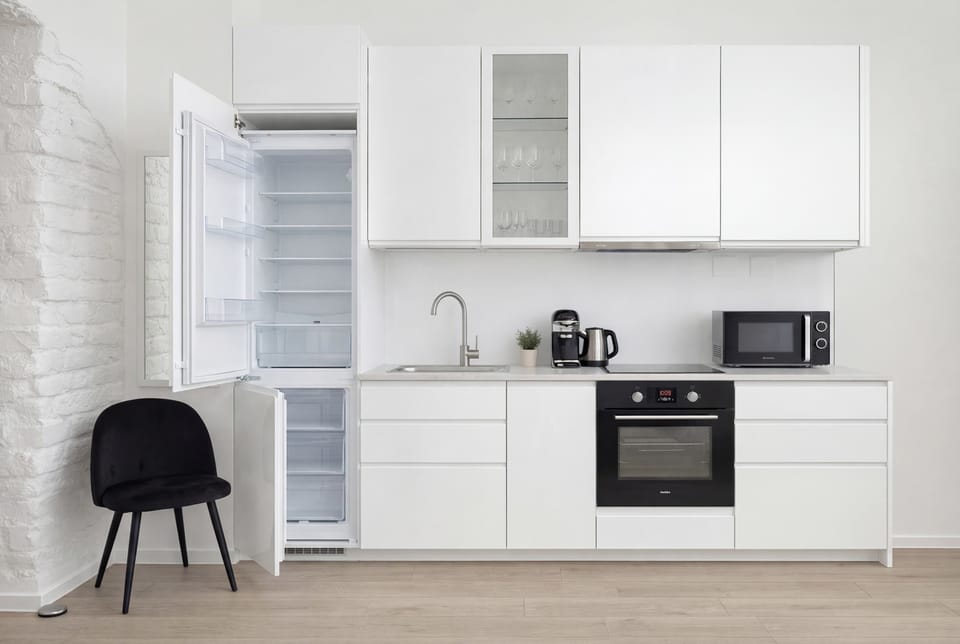 A frontal view of the kitchen displays white, handleless cabinets and modern black appliances. The layout is compact yet highly efficient, providing plenty of storage and workspace for guests.