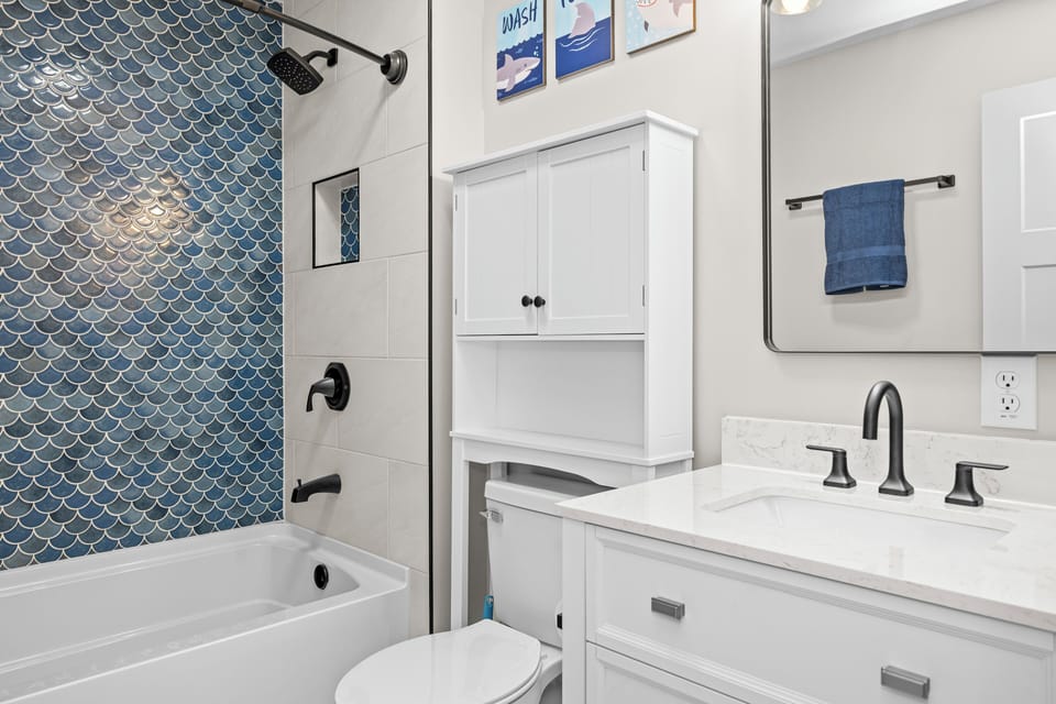 Unwind in this stylish bathroom featuring a stunning blue fish-scale tile shower, modern fixtures, and thoughtful amenities for your comfort.