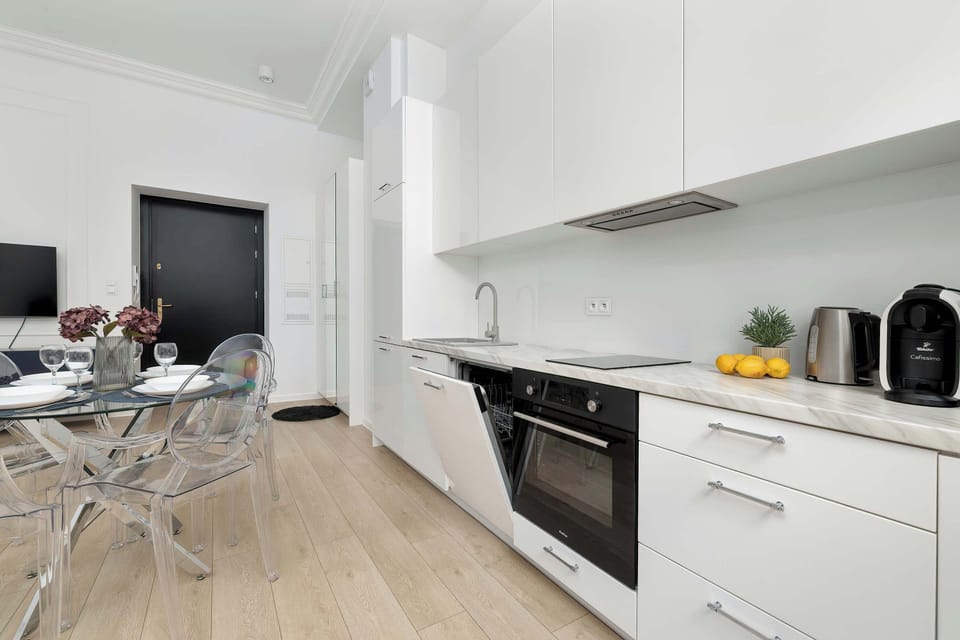 A bright kitchenette with high-quality finishes, where white cabinet fronts contrast with black details on the appliances. The ergonomic cabinet layout provides ample storage space.