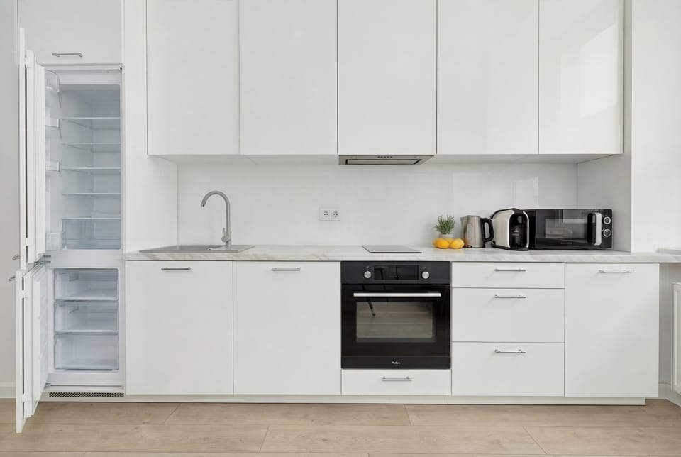 A front view of the minimalist kitchen, where the refrigerator is concealed within sleek white cabinetry. The appliances include a modern oven and an induction cooktop, ensuring full functionality.