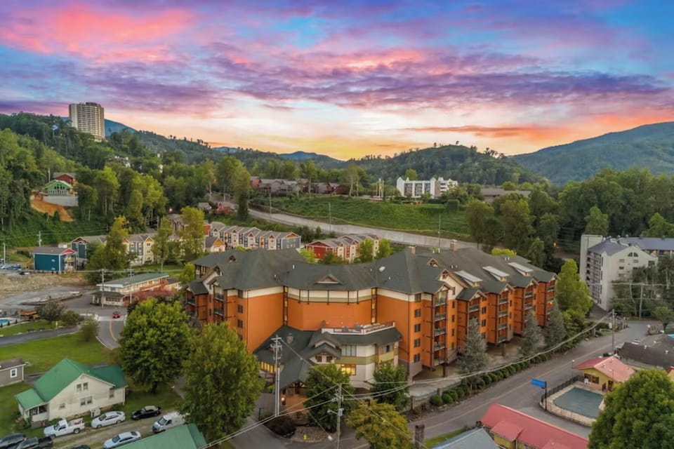 Mountain resort nestled in scenic valley with vibrant sunset skies painting the surrounding peaks and forested hills.