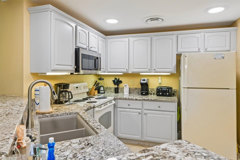 Cook your favorite meals in this fully equipped kitchen with granite counters, white cabinets, and all essential appliances for your stay.
