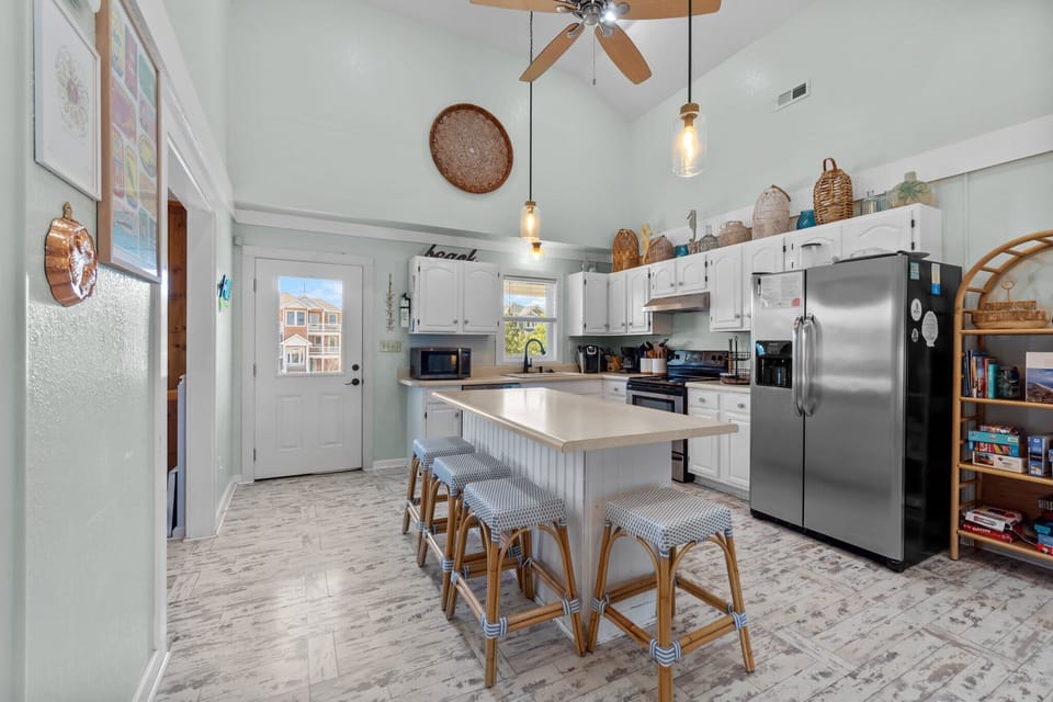 Spacious Kitchen w/ Stainless Steel Refrigerator, Electric Range & Oven,  Microwave, Sink, Cooking Utensils, Center Island w/ Bar Seating, and White Cabinetry