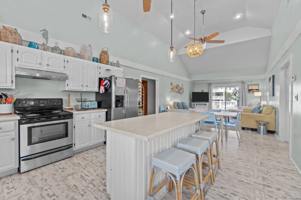 Spacious Kitchen w/ Stainless Steel Refrigerator, Electric Range & Oven,  Microwave, Sink, Cooking Utensils, Center Island w/ Bar Seating, and White Cabinetry