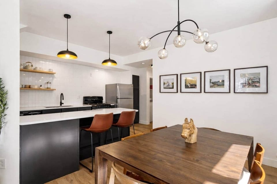 Warm, inviting dining area with a solid wood table, modern lighting, and curated artwork—perfect for shared meals and easy connection to the kitchen.