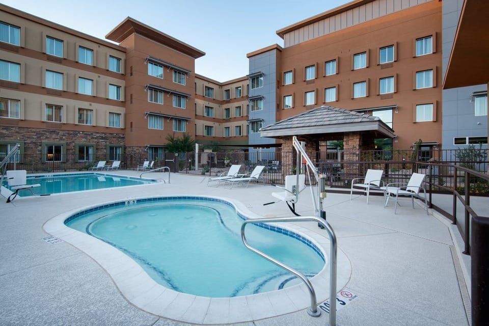 Outdoor pool with an attached hot tub, shaded gazebo, and white lounge chairs