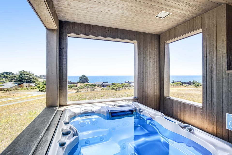 Soak in the private hot tub while enjoying stunning ocean views, the perfect way to unwind under the clear coastal skies.