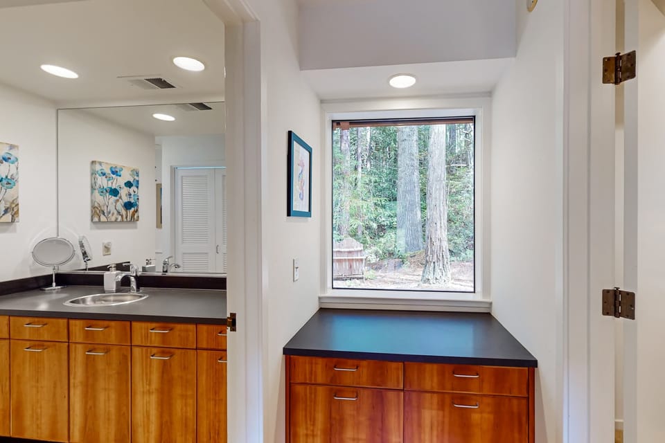 Refresh in the well-appointed bathroom, where a window frames a glimpse of towering trees, adding a touch of nature to your routine.