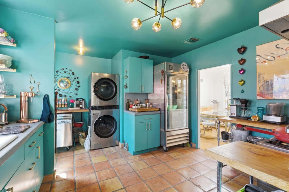The kitchen keeps going: stacked washer/dryer, glass-front beverage fridge, Sputnik chandelier, terracotta tile floor. A Sputnik light in a teal laundry room is exactly the kind of detail this house does best.
