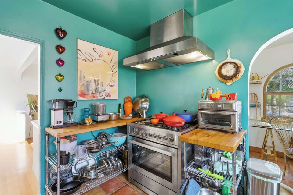 The fully-equipped kitchen: teal walls, professional stainless range with hood, butcher block counters, and everything you need to cook a proper meal — from cast iron to a toaster oven.