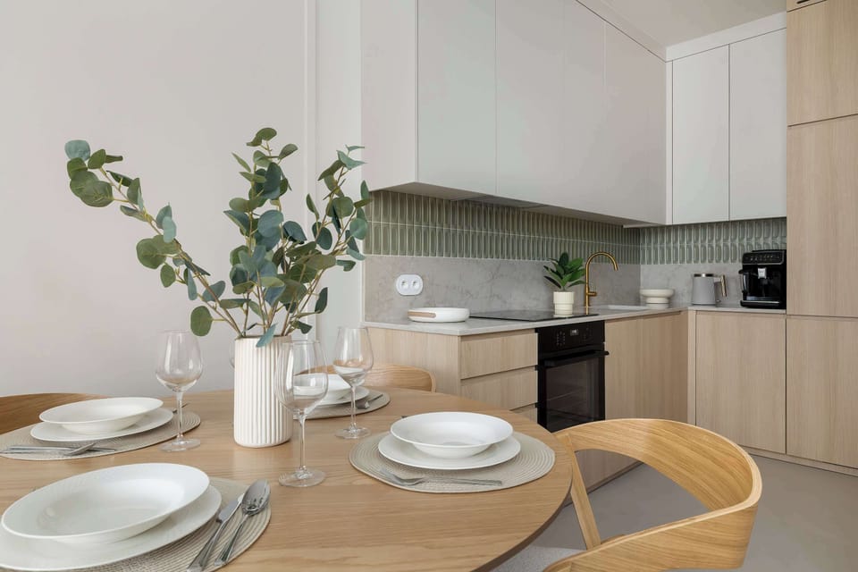 A culinary workspace features a black built-in oven and a white countertop with integrated lighting. A white vase with greenery adds a fresh touch to the functional kitchenette and dining design.