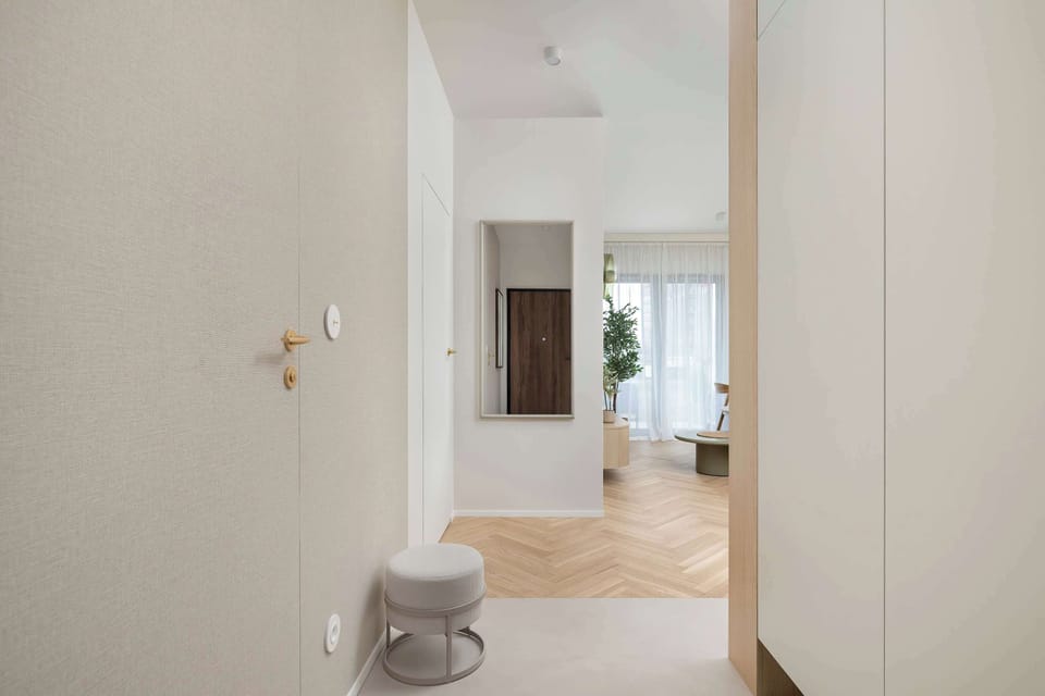A modern entryway provides a view into the bright living area, framed by a light wood wall panel. The clean white walls and polished flooring create a welcoming transition into the home.