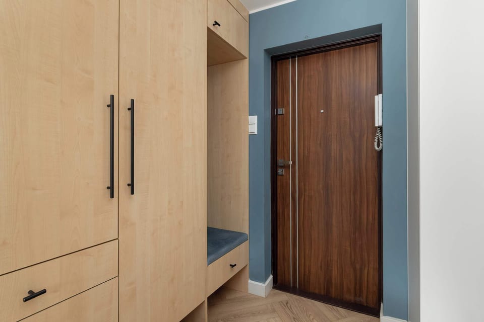 An entry hallway with a wooden wardrobe offering storage space and a solid front door. The area is neat and practical, designed for everyday convenience.