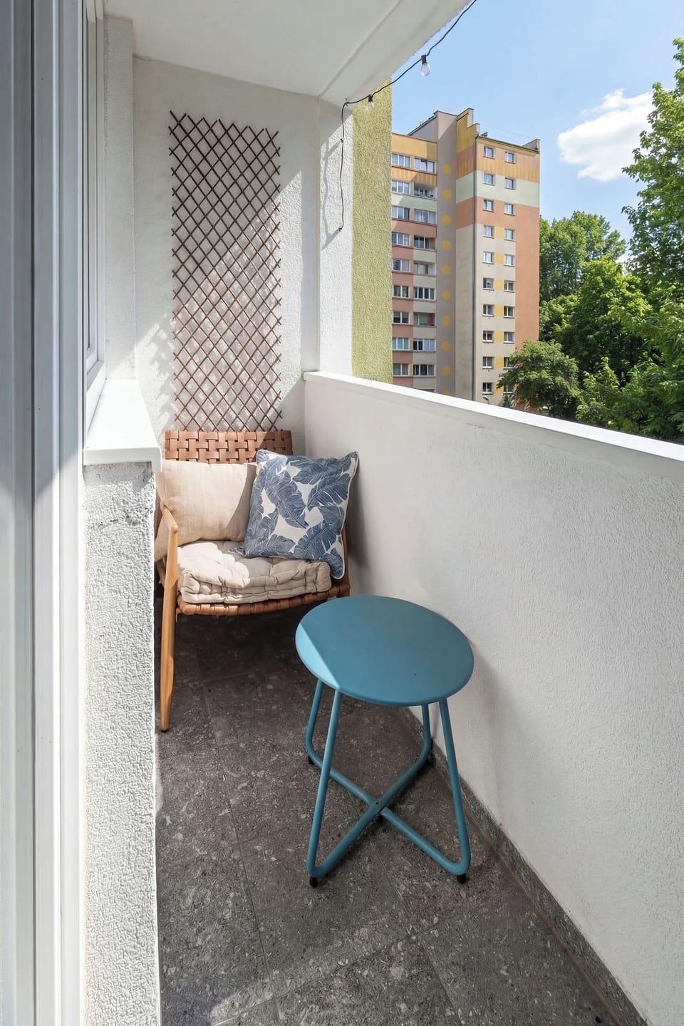 Balcony with a small table and chair, perfect for enjoying a morning coffee. The view opens up to neighboring buildings, adding an urban atmosphere.