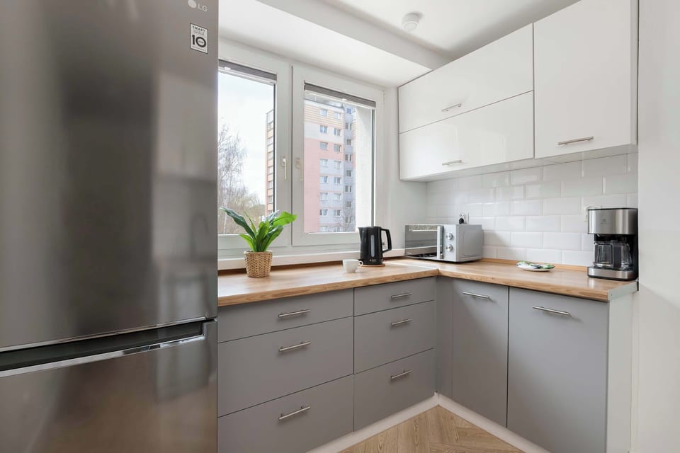 A modern kitchen with white cabinetry, wooden countertops, and built-in appliances, including an oven and a stovetop. A large window above the counter brings in natural light, making the space feel bright and practical.