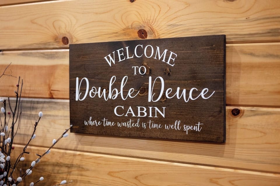 A warm wooden welcome sign greets you at Double Deuce Cabin, where rustic charm meets relaxation.