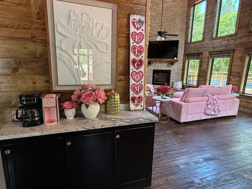 Relax in your spacious living area with soaring ceilings, cozy fireplace, and charming wood accents. Enjoy coffee from your in-room setup and unwind on plush pink seating as natural light pours through tall windows.