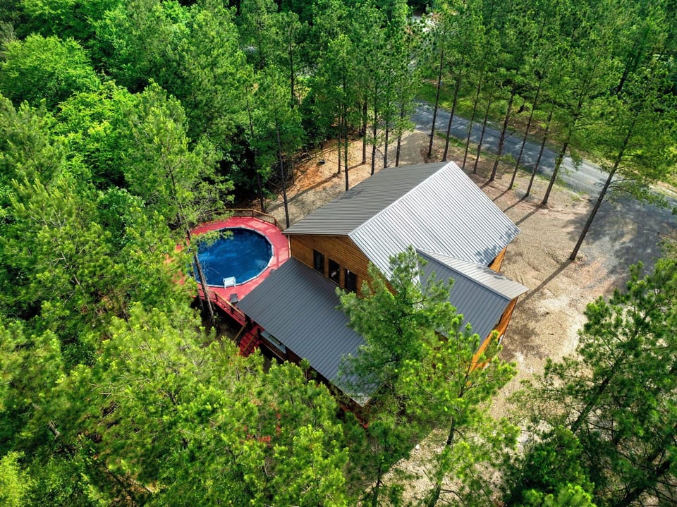 Aerial view of a secluded woodland cabin featuring a private pool, surrounded by lush forest and offering peaceful natural privacy.