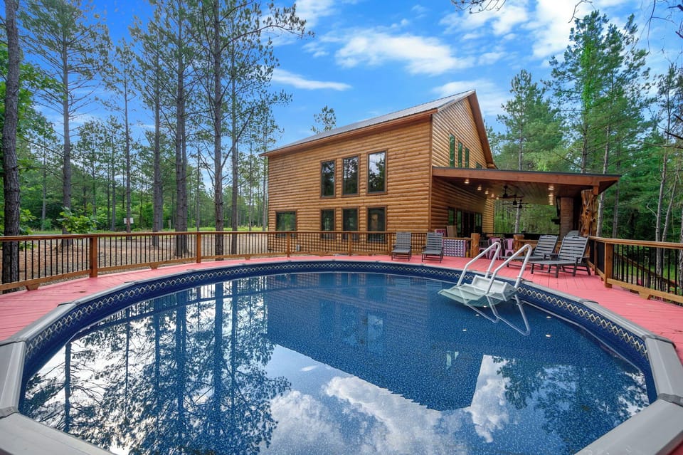 A private above-ground pool surrounded by expansive decking with lounge chairs overlooks this beautiful log cabin nestled among tall pines—your own secluded retreat in nature.