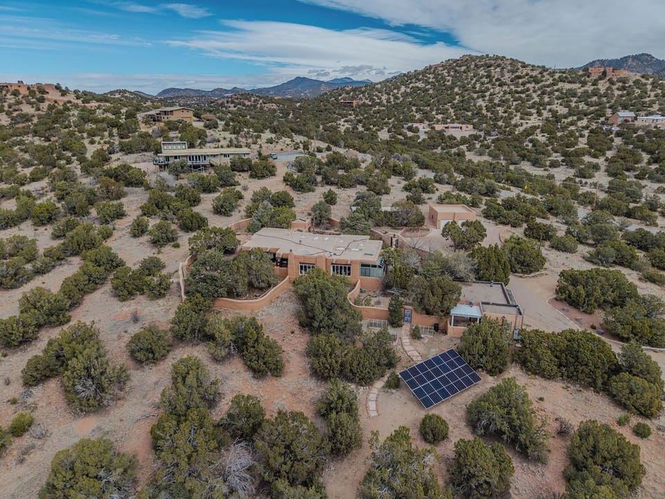 Aerial view of a secluded desert retreat nestled among rolling hills and natural vegetation in a peaceful mountain setting.