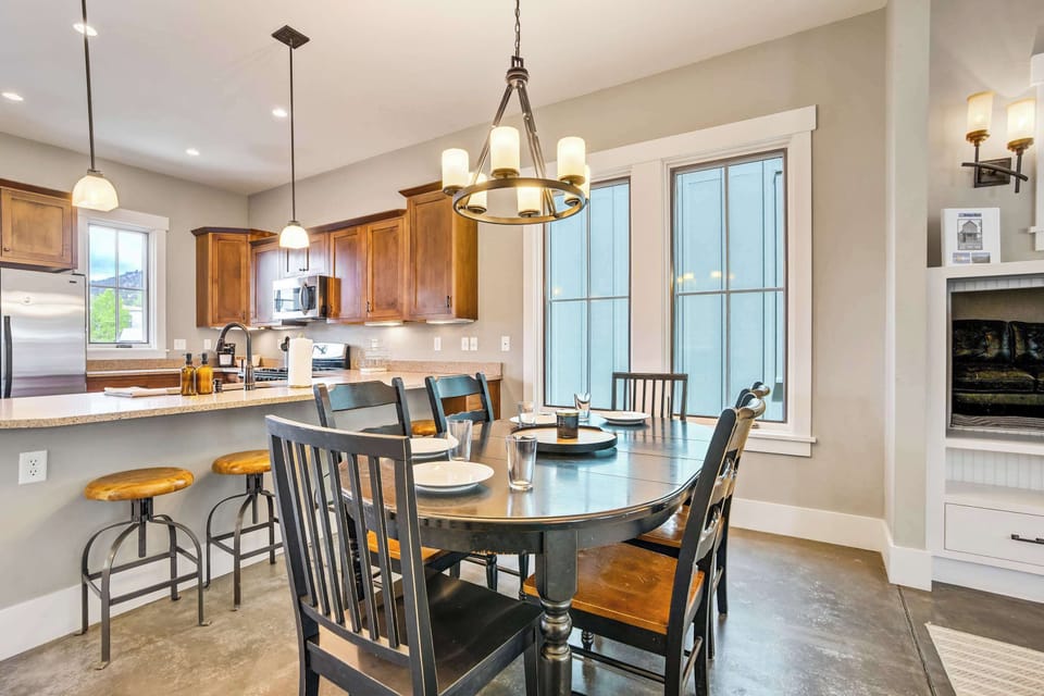 The dining area and kitchen flow together seamlessly, with the dark oval table beneath a candle-style chandelier, warm wood cabinetry, and French doors bringing in natural light from the backyard beyond.