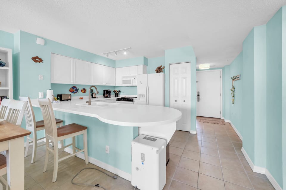 Your bright coastal kitchen invites culinary adventures with its spacious layout, modern appliances, and charming breakfast bar perfect for morning coffee.
