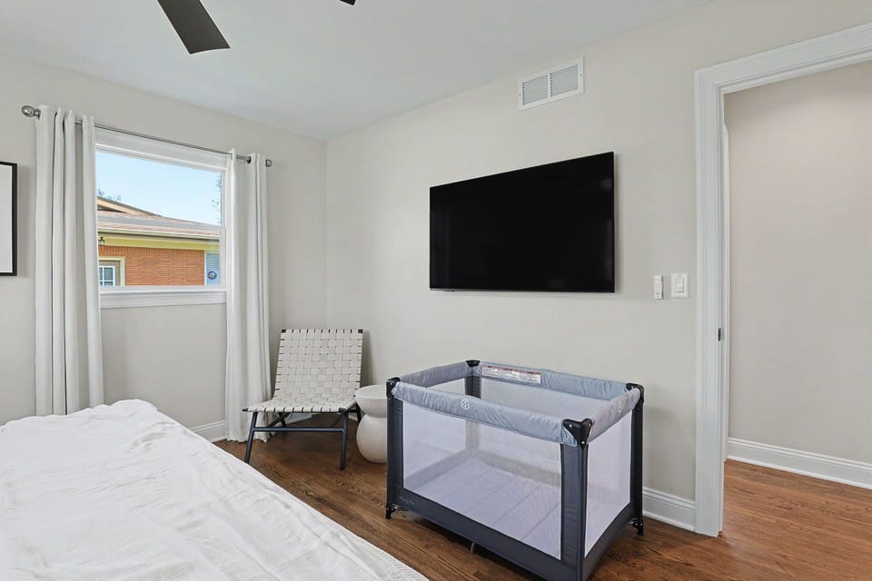 Bright bedroom with wall TV & pack ’n play—family‑ready comfort