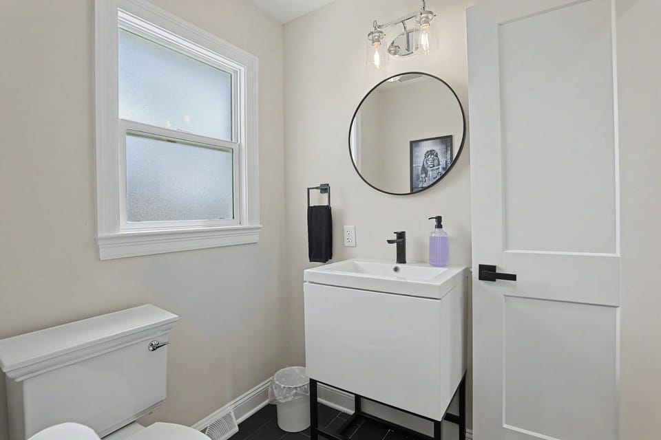 Crisp modern bath with frosted window, round mirror & black accents