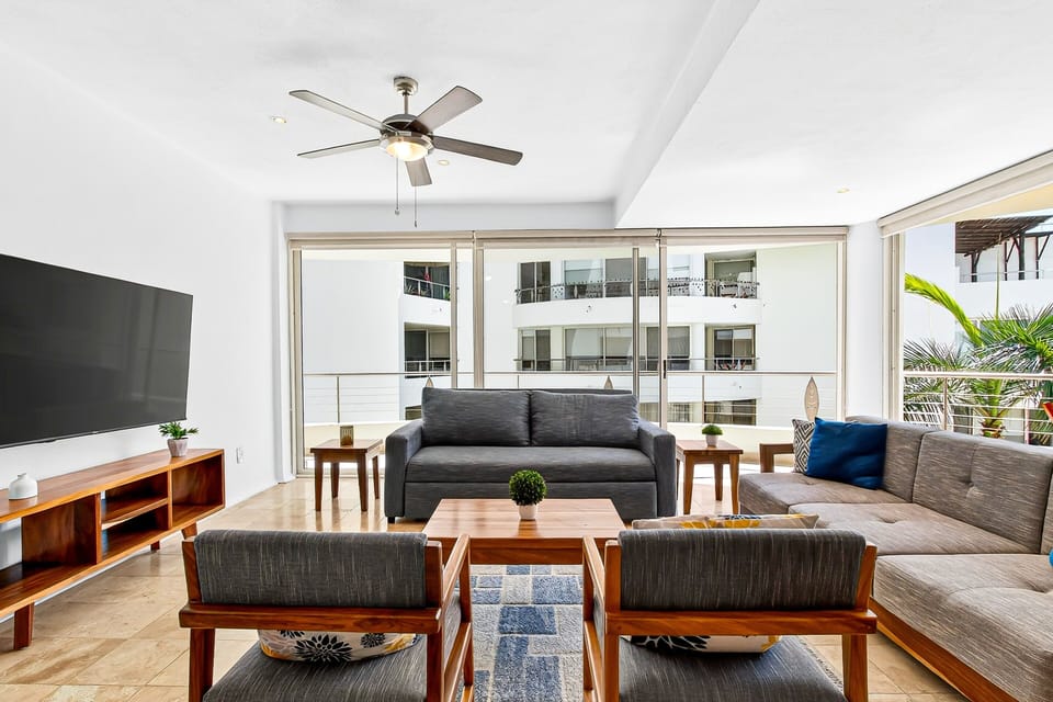 Relax in this bright and spacious living room featuring comfortable seating, large windows, and a welcoming open layout. Perfect for gathering, streaming your favorite shows, or unwinding after the beach.
