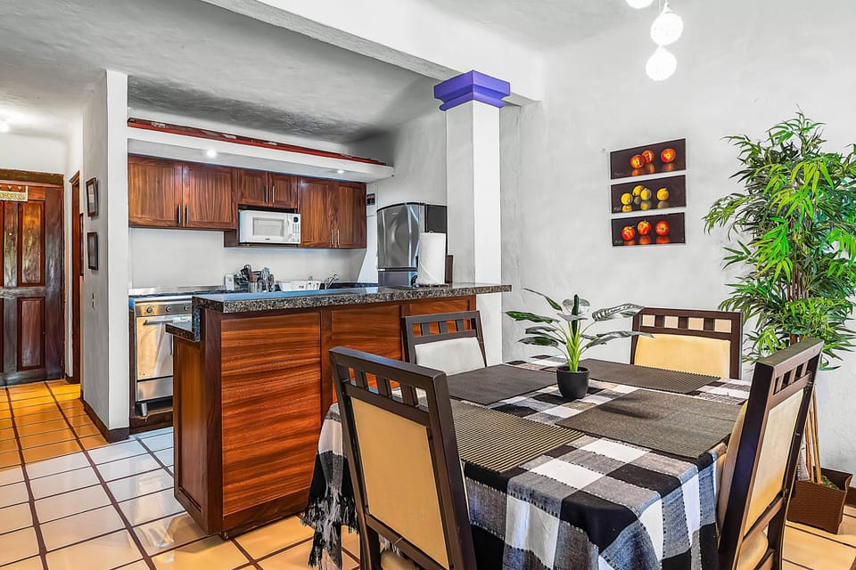Open-concept kitchen featuring rich wood cabinetry, a granite breakfast bar, and stainless steel appliances, seamlessly connecting to a charming dining table with a checkered cloth.