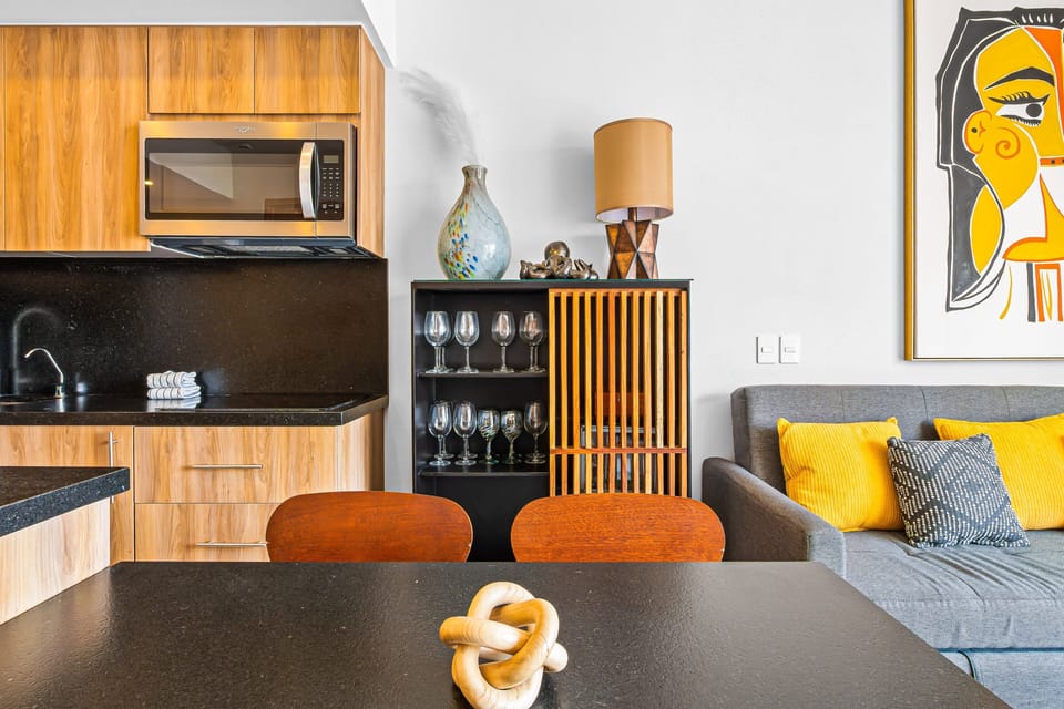 Stylish open-plan living area featuring a custom kitchenette, mid-century modern dining, and a cozy lounge adorned with bold, contemporary art. Perfect for a chic and comfortable coastal getaway.