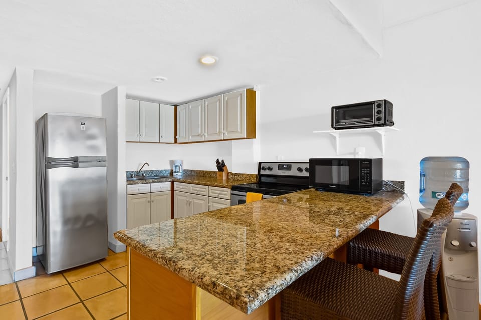 Fully equipped kitchen featuring granite countertops, full-size appliances, and a convenient breakfast bar with seating—perfect for casual meals and easy everyday cooking.