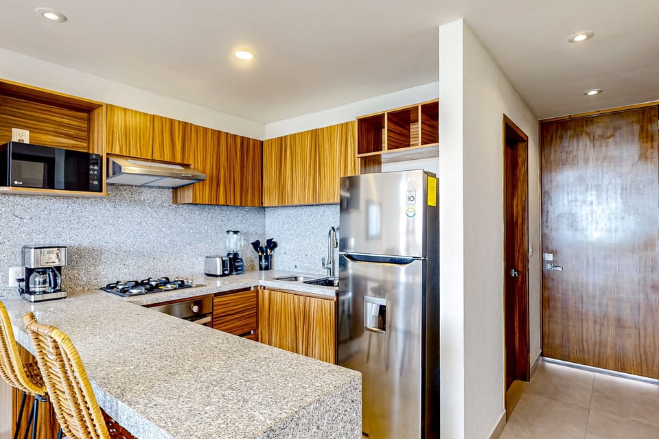 Modern kitchen with sleek countertops, warm wood cabinetry, and full-size appliances including stove, oven, microwave, and fridge. Perfectly designed for easy cooking and everyday comfort.