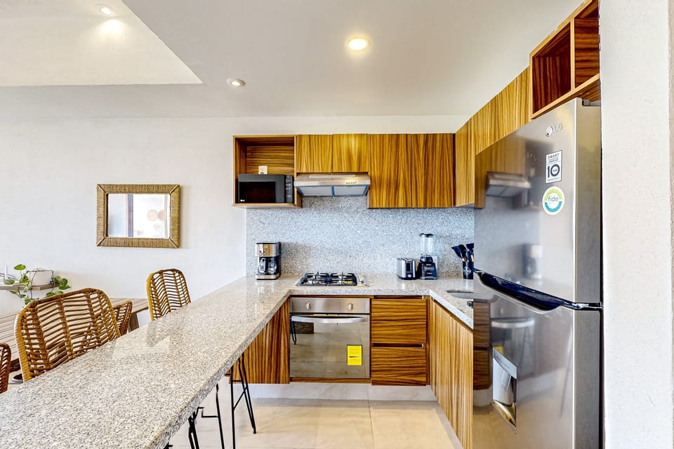 Modern kitchen with sleek countertops, warm wood cabinetry, and full-size appliances including stove, oven, microwave, and fridge. Perfectly designed for easy cooking and everyday comfort.