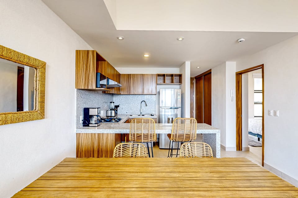 Bright open-concept kitchen with sleek finishes, breakfast bar seating, and a spacious wooden dining table. Fully equipped with essentials and stylish touches—perfect for cooking, dining, and gathering in comfort.