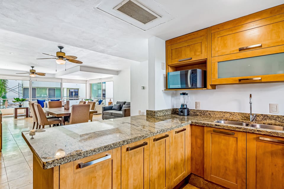 Stylish kitchen with granite breakfast bar, wood cabinetry, microwave, and open sightlines into dining and living spaces. Great for entertaining.