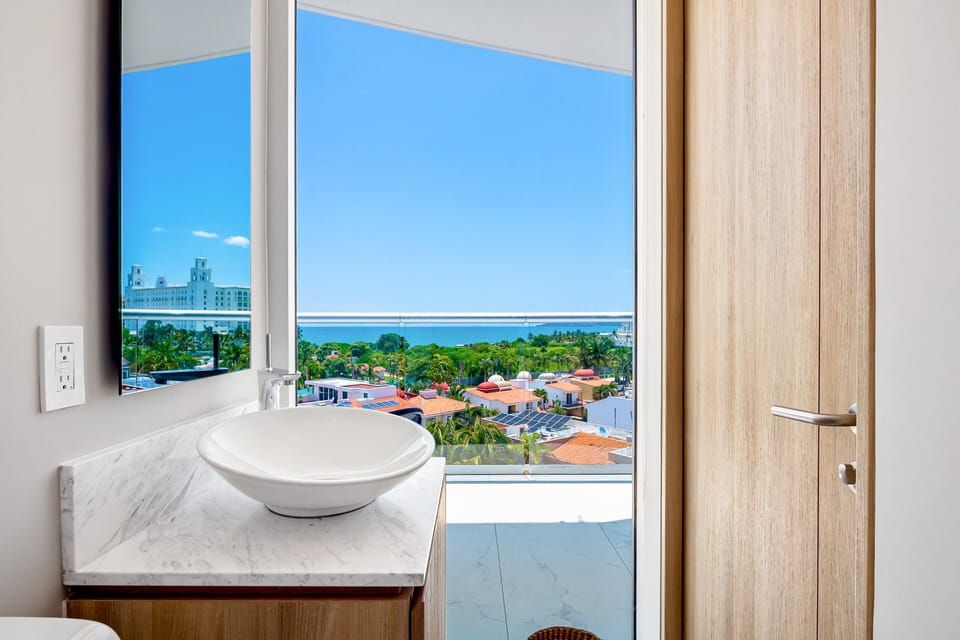 Bright bathroom featuring modern finishes, a sleek vanity, and a unique ocean-view window that brings natural light into the space.