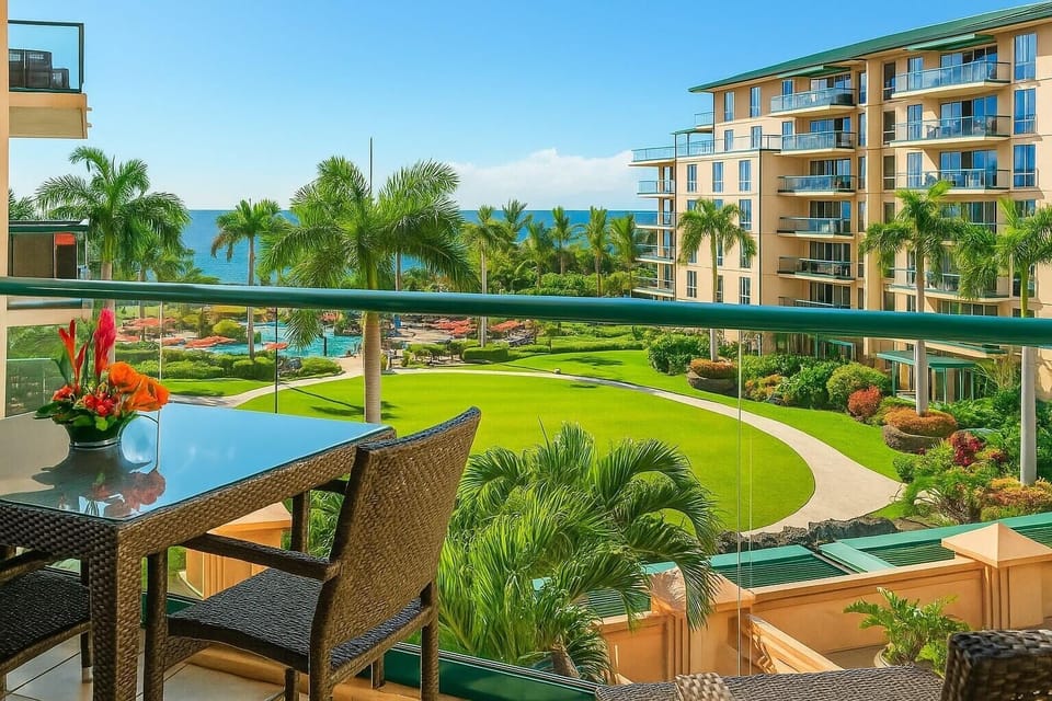 Scenic lanai dining with lush resort landscaping, mountain-lined horizon, and distant ocean sparkle. HKH-423