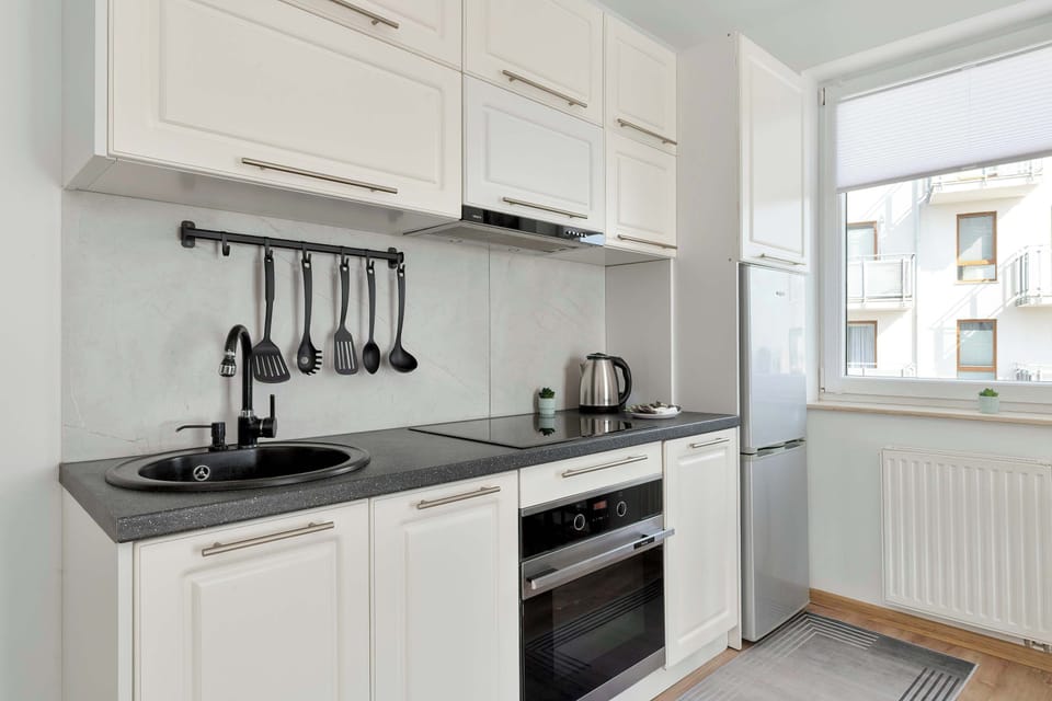 The compact kitchen area features a modern cooktop, a stylish black sink with a gooseneck faucet, and white cabinetry. A small window provides a view of the outdoors while brightening the workspace.