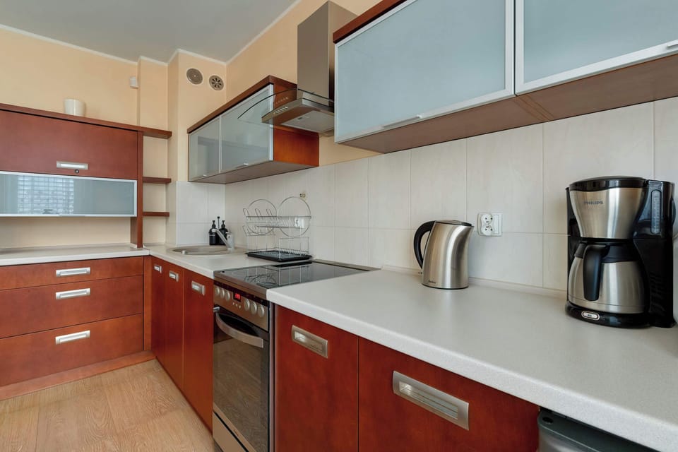 The kitchenette view highlights the inclusion of a stainless steel kettle and a professional coffee maker on the counter. Reddish-brown lower cabinets contrast elegantly with the light grey backsplash and white worktops.