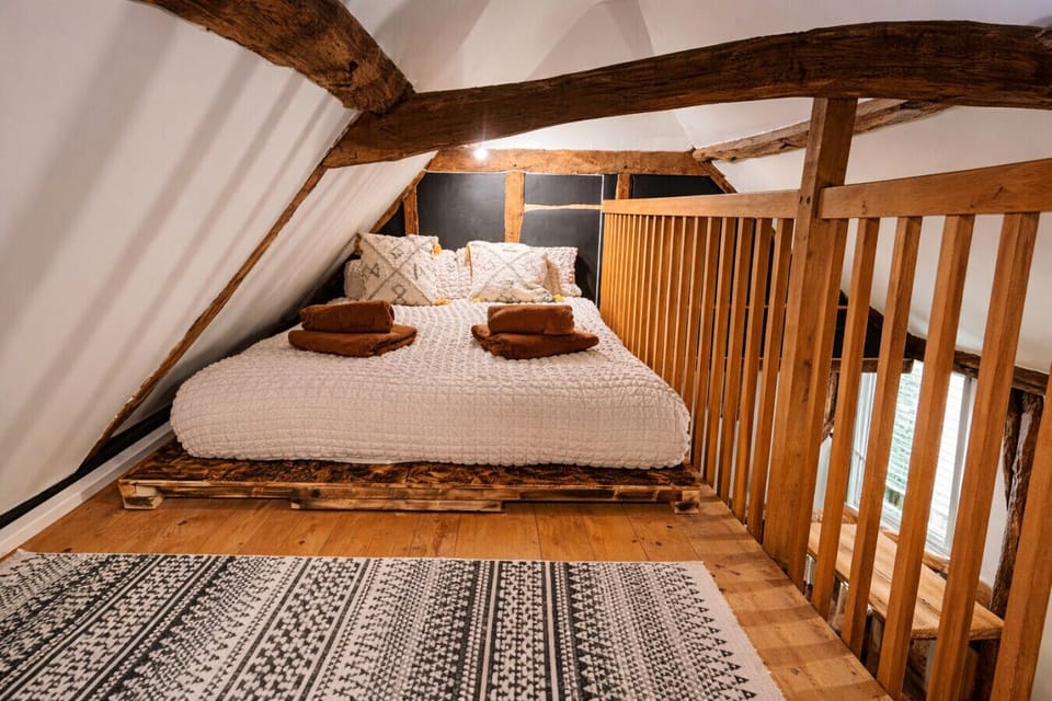 Mezzanine-level double bed with decorative cushions, exposed timber beams overhead, and wooden balustrade railings on either side.