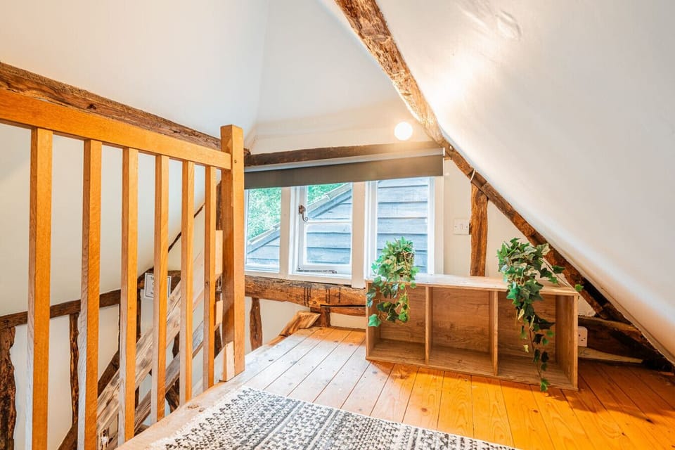The upper mezzanine space features exposed timber framing, a window providing natural light, and a small desk area.