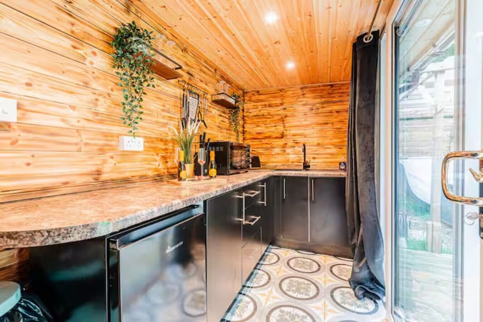 Kitchen with dark fitted units, a wooden-clad ceiling and walls, stone-effect worktop, and a patterned tile floor.