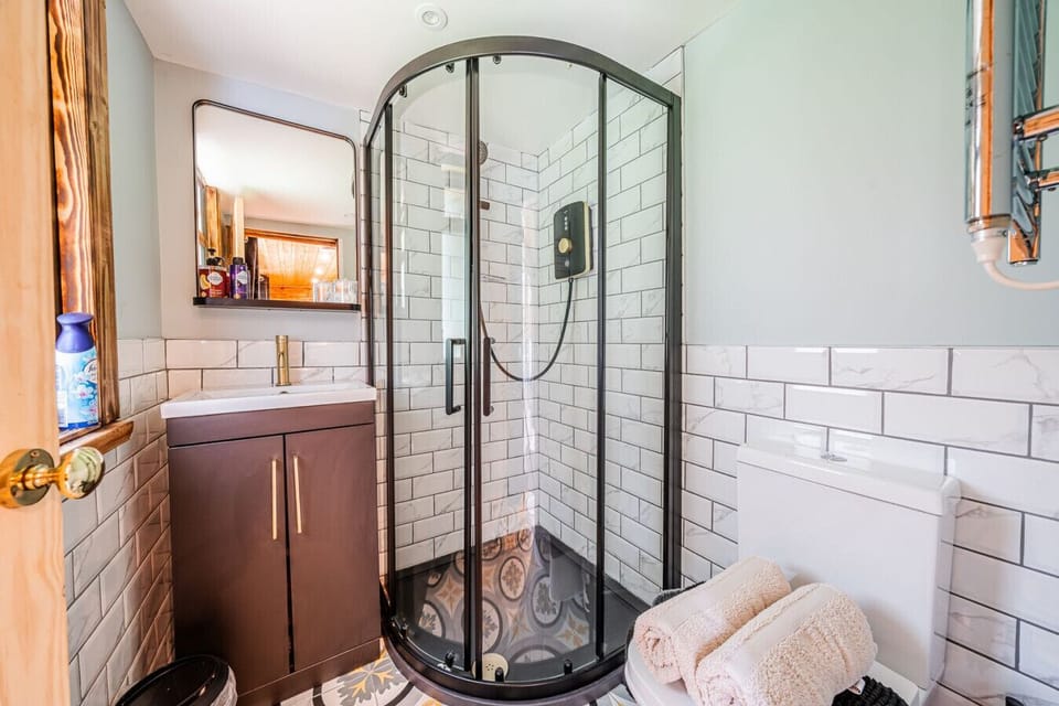Bathroom with a black-framed glass shower enclosure, white brick-effect wall tiling, dark vanity unit, and wall-mounted mirror.