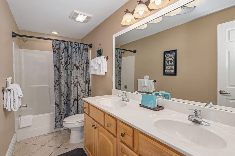 Unwind in your spacious bathroom featuring dual sinks, warm wood vanity, and relaxing tub-shower combo with fresh towels awaiting your arrival.