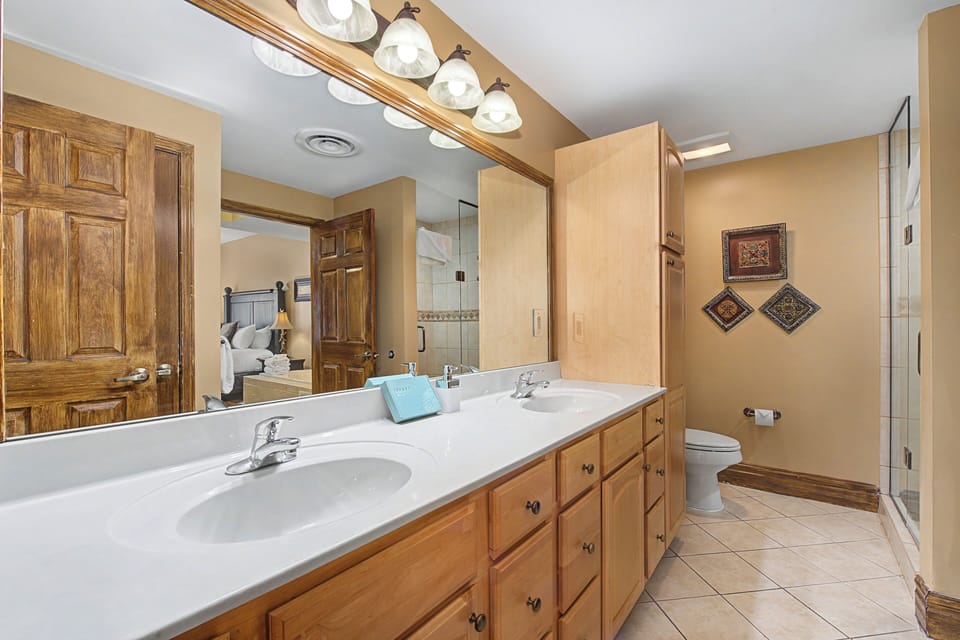 Unwind in your spacious bathroom featuring dual vanities, warm wood cabinetry, and elegant lighting for your morning routine.