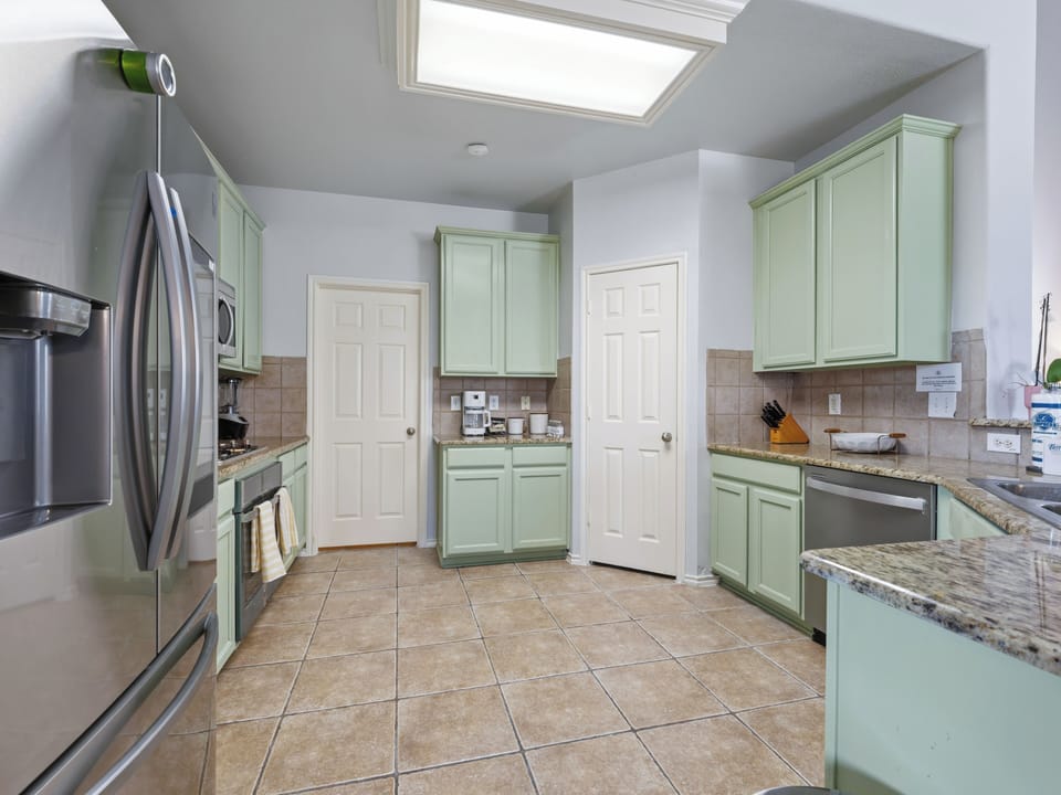 Your spacious kitchen awaits with sage-green cabinets, granite counters, and stainless appliances bathed in natural skylight.