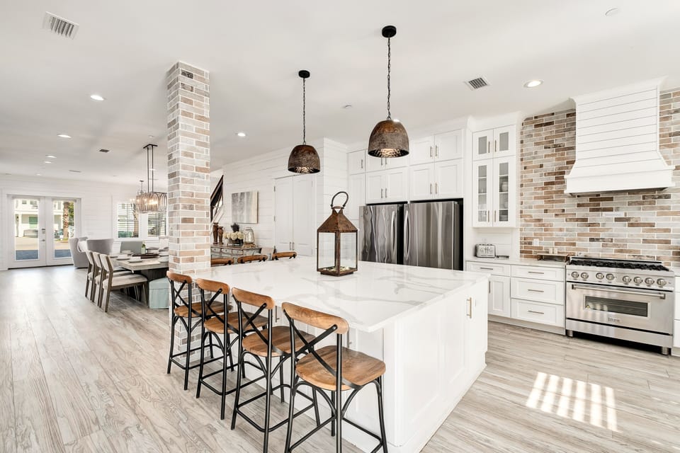 Gather around the bright kitchen island, where crisp white cabinetry meets warm brick accents and modern stainless appliances—your perfect spot for morning coffee or evening conversations.